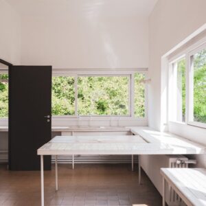 Sunlit minimalist interior space with open windows and simple furniture, located in Paris, France.